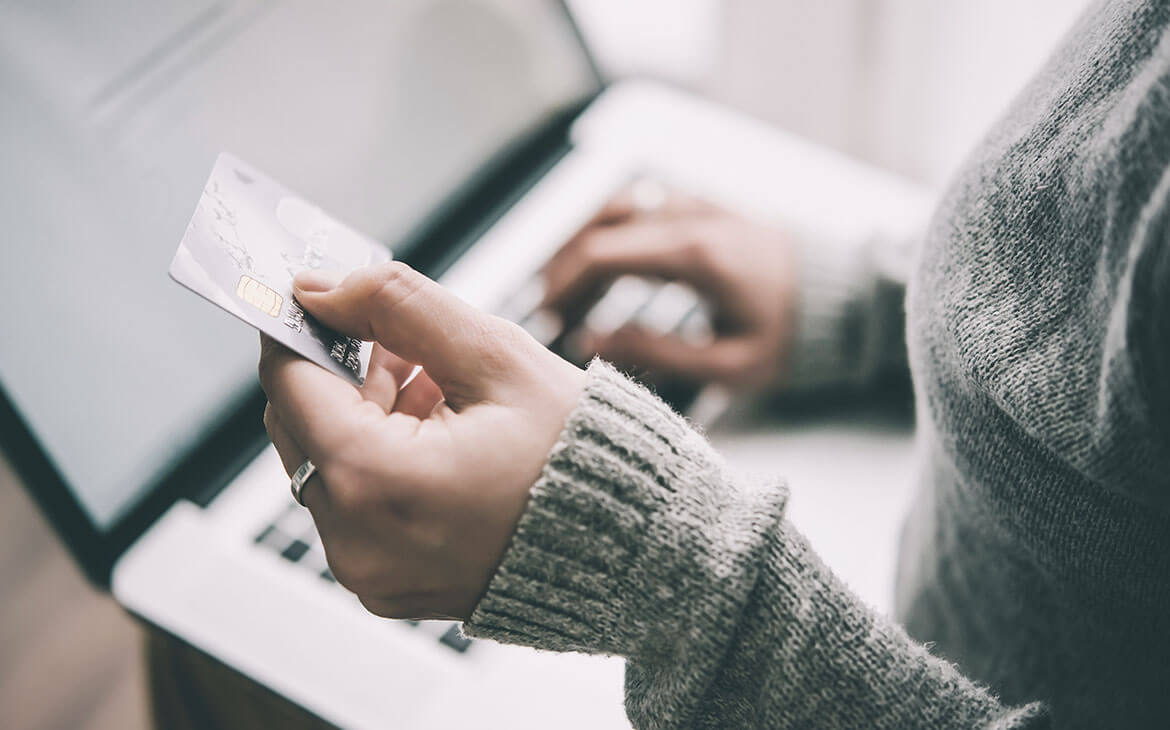 Mulher comprando online, segurando o cartão de credito em uma mao, enquanto digita com a outra.