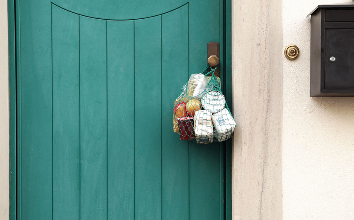 Porta fechada, com uma sacola com produtos alimenticios pendurada na massaneta. Sacola deixada por alguem em ato solidario.